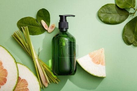 Photo for Mockup scene with empty bottle for cosmetics of pomelo and lemongrass extract and green leaves on green background. Space for design. Beauty product design, skincare and haircare - Royalty Free Image