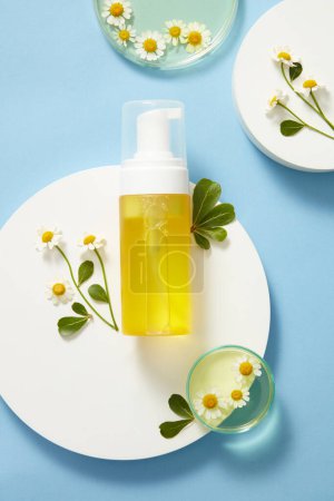 Mockup scene with empty bottle of feverfew extract, have antioxidant properties. Bottle put on white podium, fresh feverfew and green leaves on blue background. Space for design. Top view, flat lay.
