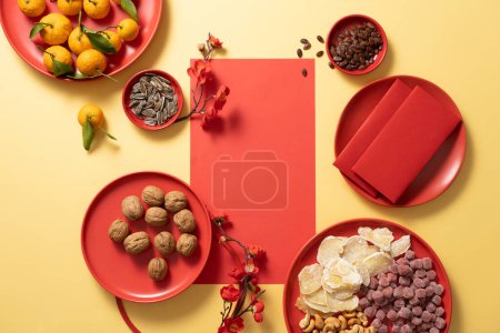 Photo for Top view, flat lay of traditional food and red envelopes on yellow background. Fresh tangerines, a tray of jam candies and nuts are placed on round red plates. Lunar New Year. Copy space - Royalty Free Image