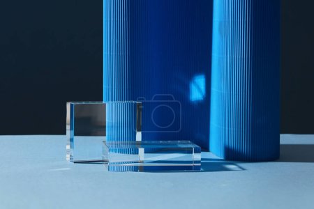 Two transparent geometric blank podiums decorated on dark background. Blue paper corrugated to create a wavy shape. Space for advertising products display