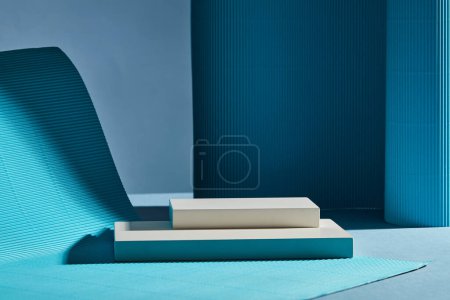 Téléchargez les photos : Deux podiums vides rectangulaires blancs empilés sur fond sombre. Les plis bleus forment le mur ondulé doux et le tapis. Concept minimal pour la présentation des produits - en image libre de droit