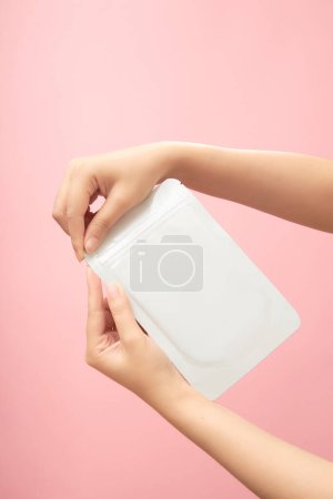 Photo for Front view of two female hands holding a mask packaging, ready to tear, on pastel pink background. Mockup for package design, daily routine skincare, beauty cosmetic product. - Royalty Free Image
