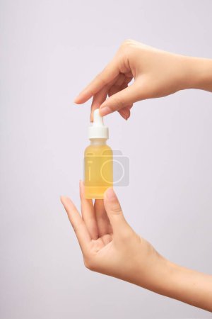 Two female hands holding an empty glass without label containing yellow essence on white background. Mockup for cosmetic or serum product, space for your design