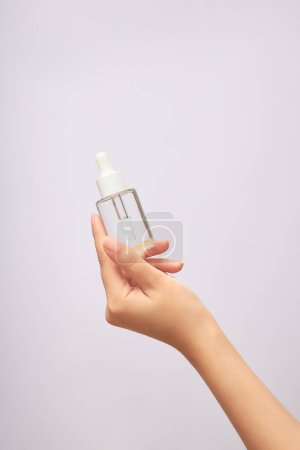 Beauty and skincare concept. Woman's hand holding a glass cosmetic bottle with empty label for design. Isolated on white background with copy space