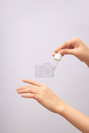 Women's hands hold pipette with cosmetic serum on light background. Close-up, copy space. Concept of skin care, beauty cosmetic product