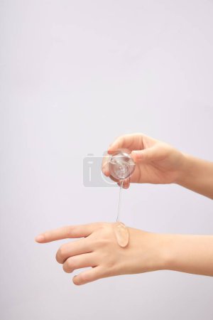 Front view of female hand pouring transparent essence on back of other hand on light background. Mockup scene for cosmetic product, daily skin care routine.