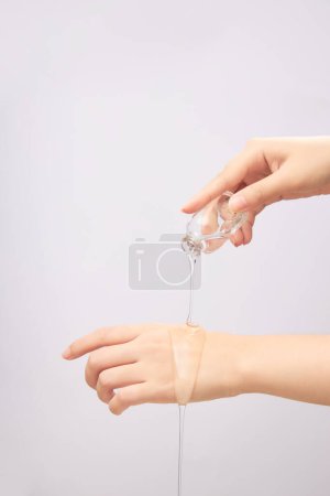 Female hand pouring transparent essence on back of other hand on white background. Beauty cosmetic product for skin care concept. Mockup for package design