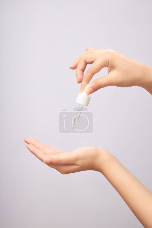 Woman's hand holding pipette, drop by drop of serum on palm on light background. Advertising photo for cosmetic or serum product, skincare concept.