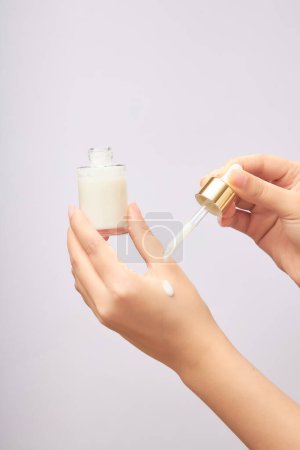 Woman drops serum on her hand. Holding an unlabeled serum bottle on a light background. Scene for advertising cosmetic product, mockup for package design
