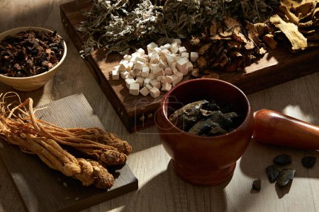 Top view of traditional herbs on wooden tray, podium, bowl, mortar and pestle on wooden table background. Herbal collection for the preparation of a tonic drink