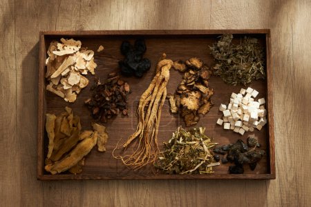 Top view of traditional Chinese herbs placed on a dark wooden tray, on wooden table background. Scene for medicine advertising, photography traditional medicine content