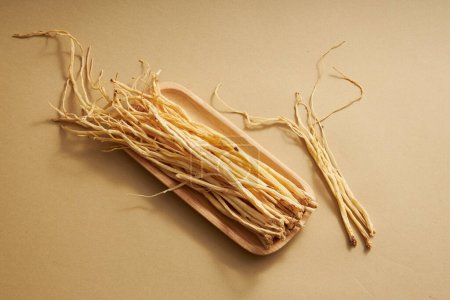 Foto de Algunas raíces de la pilosa asiabell en platos de madera sobre fondo marrón claro. La medicina tradicional china tiene el efecto de mejorar la salud y mejorar la resistencia - Imagen libre de derechos