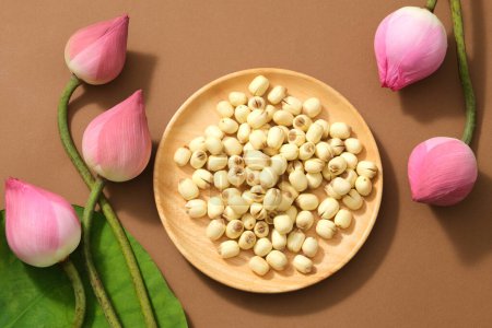 Photo for Top view of (Nelumbo nucifera) fresh lotus buds, green leaf and lotus seeds on wooden dish on brown background. Lotus flower is the Vietnamese national flower. - Royalty Free Image