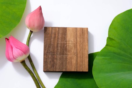 Wooden empty platform with pink lotus buds and lotus green leaves on white background. Top view of background for advertising product contains lotus seed ingredients. (Nelumbo nucifera)