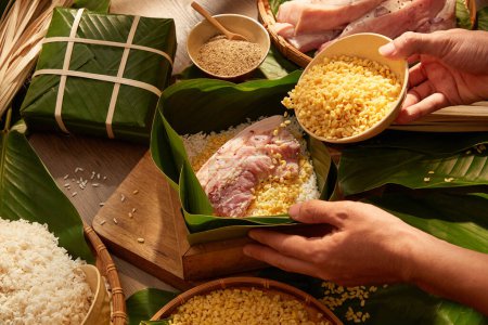 Photo for Hands putting mung beans in box lined with dong leaves when making sticky rice cake. Background for holiday food advertising , top view - Royalty Free Image
