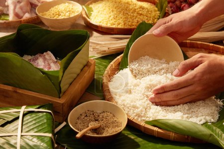 Photo for Hands putting white rice in box lined with dong leaves when making sticky rice cake (Chung cake). Traditional lunar new year food - Royalty Free Image