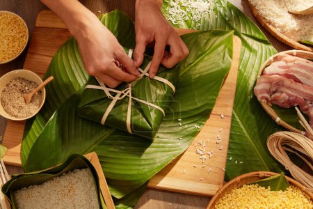 Photo for Hands of person making traditional sticky rice cakes for Chinese New Year celebration. All ingredients are placed on a wooden table. Top view - Royalty Free Image