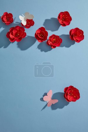 Téléchargez les photos : Vue du dessus des fleurs en papier rouge, des papillons blancs et roses sur fond bleu. Blank pour une carte publicitaire ou une invitation. Concept de fleur de printemps. Pose plate. - en image libre de droit