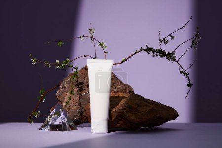 Photo for Front view of white plastic tube with facial moisturizer cream or facial cleanser on purple background. Brown stone with white flower as a highlight. - Royalty Free Image