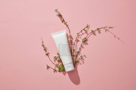 Photo for White empty plastic tube with facial moisturizer cream or facial cleanser and small branches flower on pink background. Mockup for presentation of cosmetic products. Top view, flat lay. - Royalty Free Image