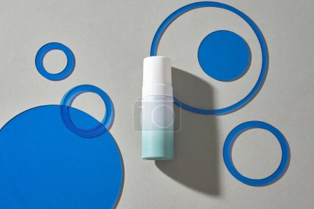 Téléchargez les photos : Vue du dessus de la bouteille cosmétique vide et des cercles géométriques bleus se détachent sur fond gris, position plate. - en image libre de droit