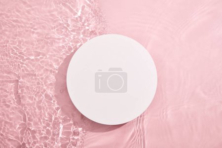 Photo for White circular empty podium, set on a pink background with water and tiny ripples. Blank for cosmetics presentation. Top view, flat lay cosmetic mockup. - Royalty Free Image