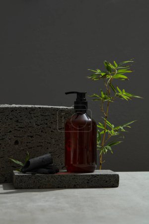 Photo for Empty glass bottle on stone and bamboo charcoal. Green bamboo leaves stand out in the dark background. Advertising photo. Mockup - Royalty Free Image
