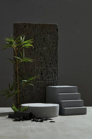Frontansicht des leeren Podiums für Displays für Produkte. Bambusblätter, Bambuskohle und Steine als Akzente auf schwarzem Hintergrund. Minimales Konzept.