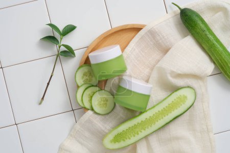 Photo for Two green jars without label are placed on a wooden dish with white towel and Cucumber slices. Cucumber (Cucumis sativus) is extremely beneficial to those with irritated and acne-prone skin - Royalty Free Image