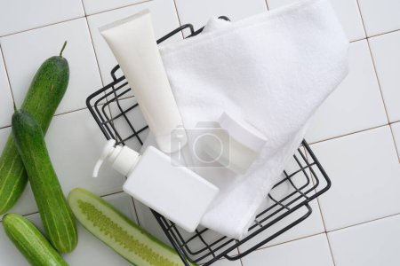 Photo for A basket with a pump bottle, a tube and a jar placed on. White mosaic tiles background. Cucumber (Cucumis sativus) has anti-inflammatory properties that can reduce skin inflammation effectively - Royalty Free Image