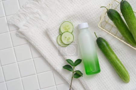 A gradient white and green bottle decorated with Cucumber slices and green leaves on a towel. Cucumber (Cucumis sativus) helps disappear dark circles and dark spots