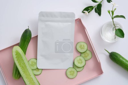 Photo for A mask sheet decorated on pink tray with Cucumber slices, a flower vase beside. The cooling and anti-inflammatory effect of Cucumber (Cucumis sativus) may help ease pain, redness, and irritation - Royalty Free Image