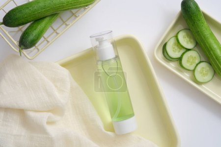 Photo for A bottle containing liquid extracted from Cucumber (Cucumis sativus) displayed on a tray with towel and a basket of Cucumber. Herb for use a cosmetic production in beauty treatment - Royalty Free Image