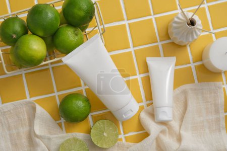 Photo for Two white tubes arranged with a basket of Lime, reed diffusers and a candle against a yellow mosaic tile background. Lime (Citrus aurantiifolia) has many advantages for health and skin - Royalty Free Image