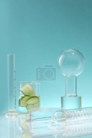 Photo for A condenser, volumetric cylinder and a beaker with Cucumber slices inside against a blue background. Cucumber (Cucumis sativus) is a source of moisture and helps the body detox - Royalty Free Image