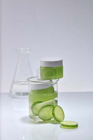 Photo for Minimal scene of a beaker containing Cucumber slices and two empty label jars with liquid. Mockup of cosmetic product extracted from Cucumber (Cucumis sativus), laboratory research content - Royalty Free Image