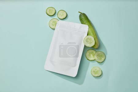 Photo for A facial mask sheet packaging placed on light blue background with several Cucumber slices. Branding mockup for skin care mask product extracted from Cucumber (Cucumis sativus) - Royalty Free Image