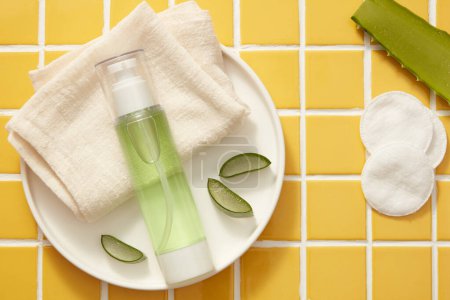 A round dish with folded towel, Aloe vera slices and a pump bottle containing green liquid, decorated with cotton pads. Aloe vera (Aloe barbadensis miller) has many benefits for skin and hair