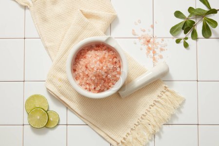Photo for A mortar filled with pink salt arranged with a pestle placed on towel, a tree branch and Lime slices displayed. Himalayan pink salt reduces sebum production and clears skin congestion - Royalty Free Image