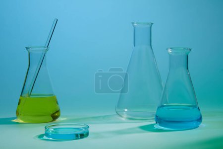 Three erlenmeyer flask filled with blue and yellow fluid. Empty area to display product. Concept of chemical, scientific experiment