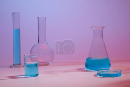 Several glassware containing blue liquid against a gradient background. Cosmetic laboratory research and development