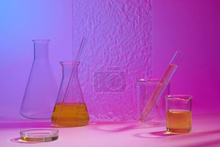 Transparent acrylic sheet decorated with conical flasks, test tubes, beakers and petri dish of orange fluid. Science advertising laboratory background