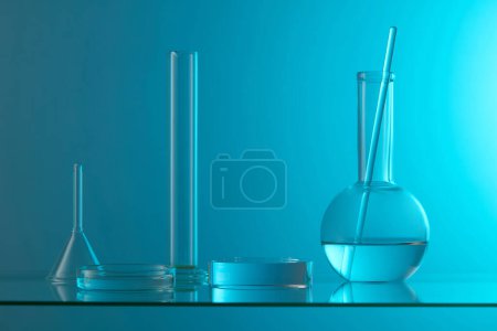 Against a blue background, a transparent arranged with some laboratory glassware on a glass table. Stage showcase on minimal podium display