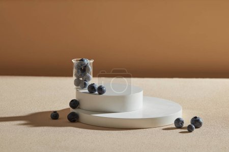 Photo for Round podium stacked with many blueberries contained inside a beaker placed on. Vacant space to display cosmetic product. Blueberries (Vaccinium Corymbosum) are high in antioxidants - Royalty Free Image