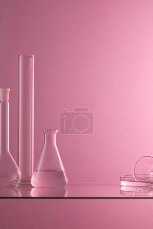 Foto de Varios artículos de vidrio de laboratorio que contienen líquido transparente se colocan en una mesa de vidrio con fondo púrpura. Espacio en blanco para mostrar el producto - Imagen libre de derechos