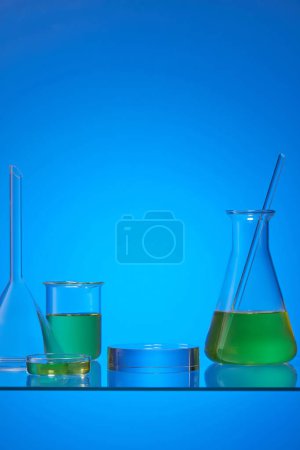 Photo for An erlenmeyer flask, petri dish and beaker filled with yellow fluid on the blue background. Empty round transparent pedestal for advertising - Royalty Free Image