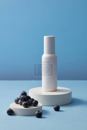 Photo for Blank label beauty bottle and some blueberries placed on two round white podiums. Blueberry (Vaccinium Corymbosum) brings nutrients and oxygen to your skin - Royalty Free Image