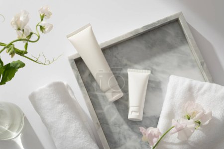 Photo for A gray marble tray with towel, flower branch and two white tube displayed on, white flower branches inside a glass transparent pot. Gentle skin care concept - Royalty Free Image