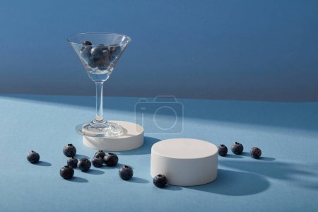 Photo for Cocktail glass containing blueberries put on a round podium with an empty podium beside. Salicylic acid in Blueberry (Vaccinium Corymbosum) restores the vibrant color of skin. - Royalty Free Image