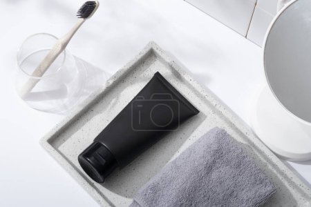 Foto de Una bandeja de mármol con un tubo negro y una toalla, un vaso con cepillo de dientes y espejo decorado en concepto de baño. Etiqueta en blanco para la maqueta del producto - Imagen libre de derechos